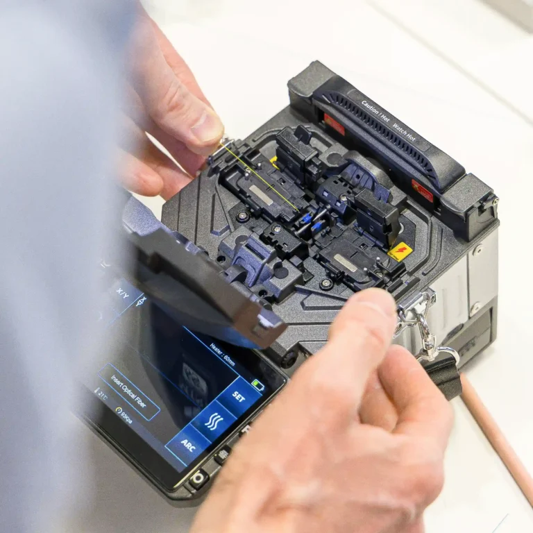 Ein Techniker von Schweinberger Glasfaser Experte führt eine feine Glasfaser präzise in ein Spleißgerät ein, um eine dauerhafte Verbindung am Glasfaseranschluss herzustellen. Diese exakte handwerkliche Arbeit ist die Grundvoraussetzung für eine verlustfreie Signalübertragung.