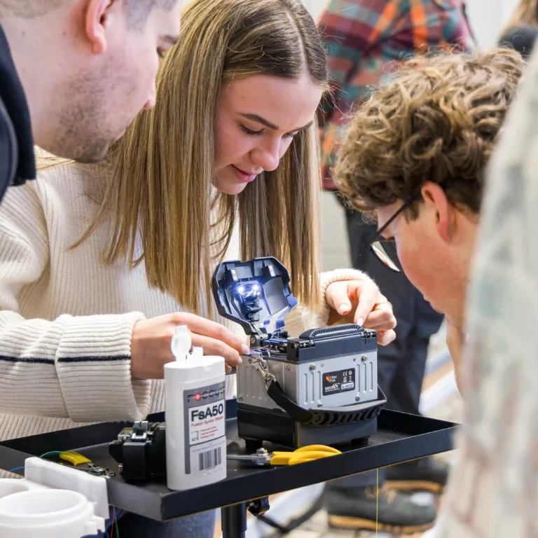 Eine Gruppe junger Talente lernt die hochpräzise Handhabung eines Spleißgeräts zur Verbindung von Lichtwellenleitern.