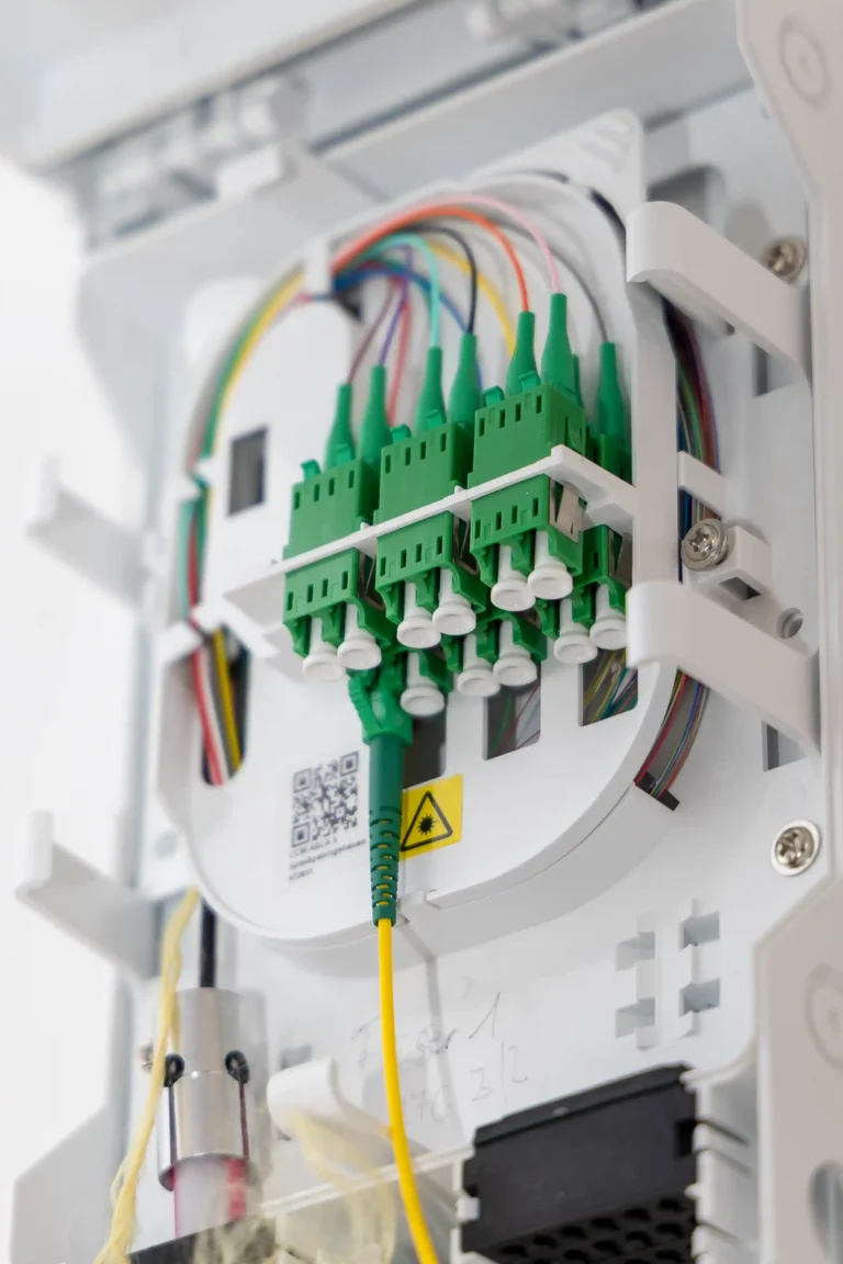 Nahansicht der Innenverkabelung eines Glasfaser-Hausanschlusses, an dem ein gelbes Messkabel zur Qualitätsprüfung angeschlossen ist.